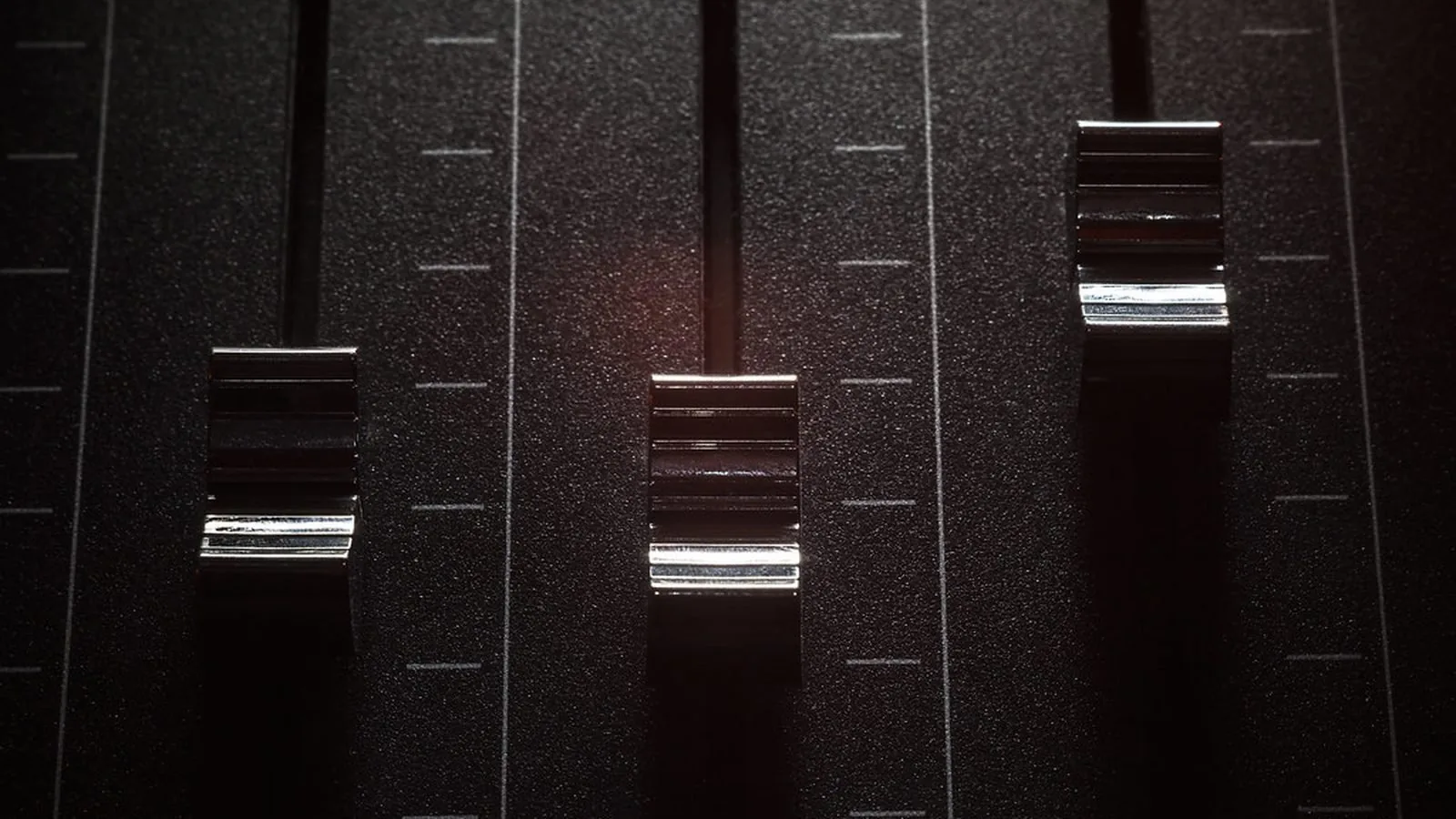 Close-up of three faders on a dark audio mixing console