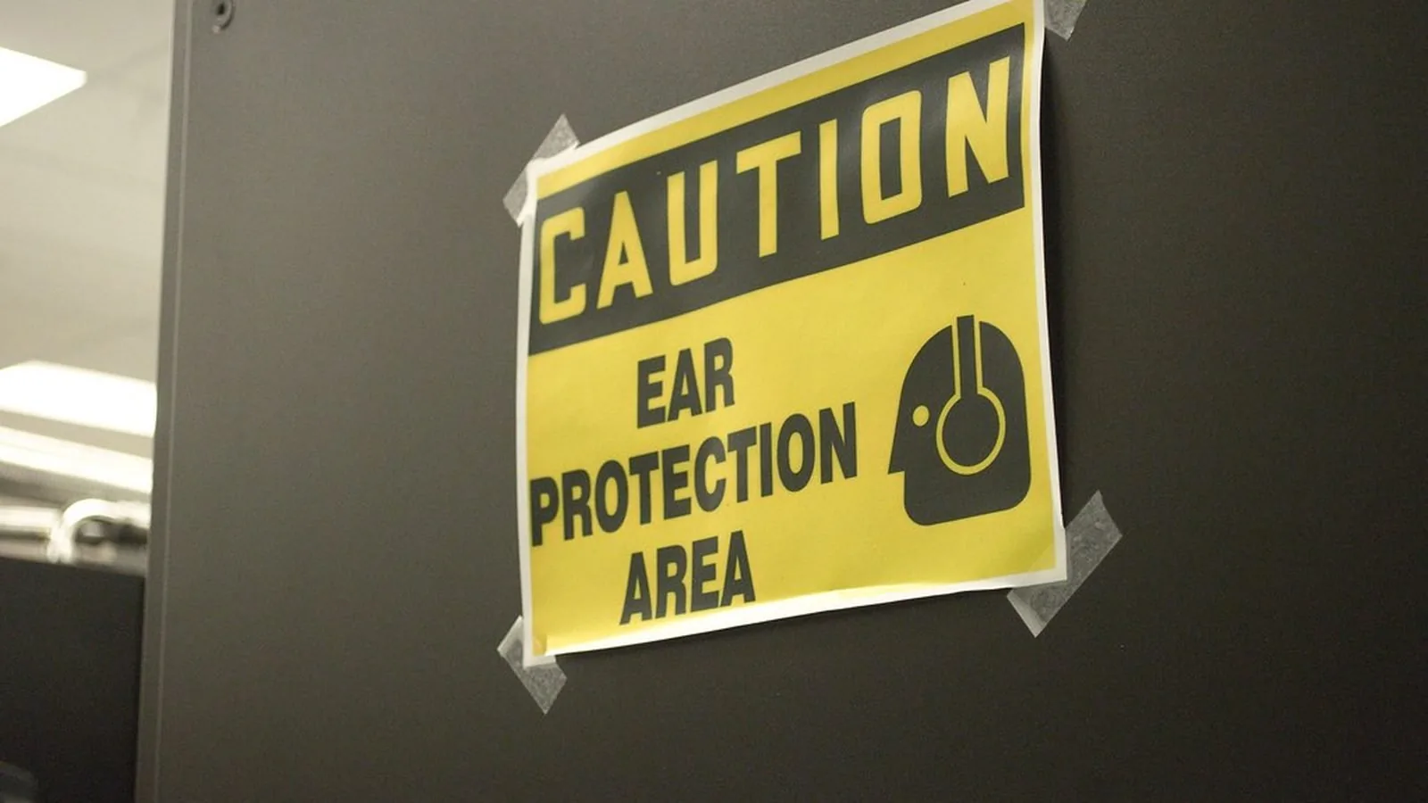 A yellow sign on a wall reading Caution, Ear Protection Area