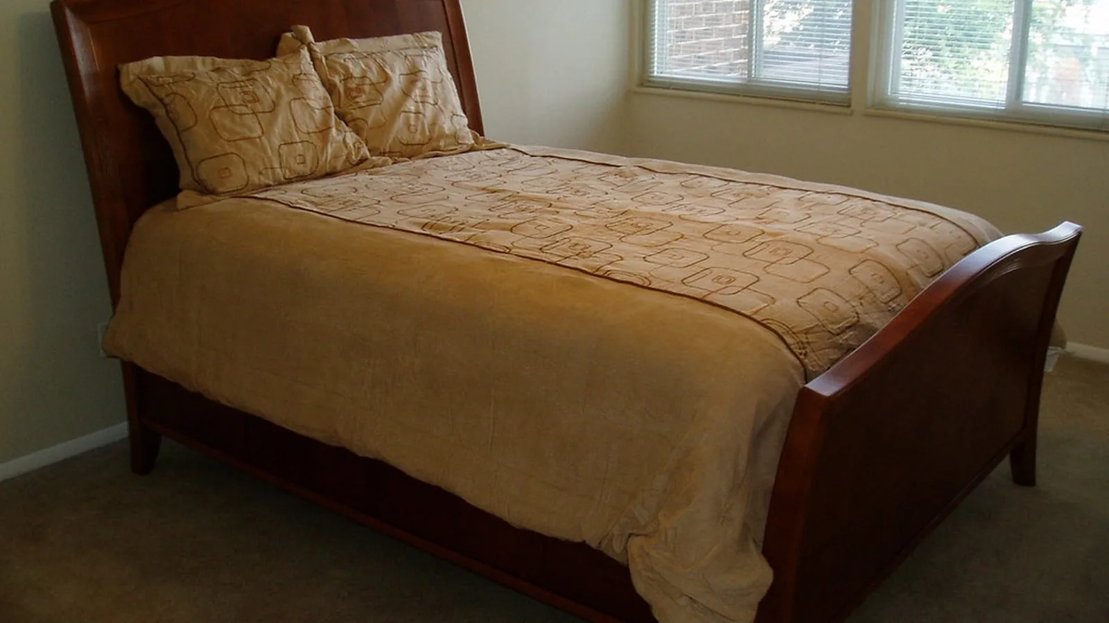 An empty made bed in a bedroom with morning light from the windows