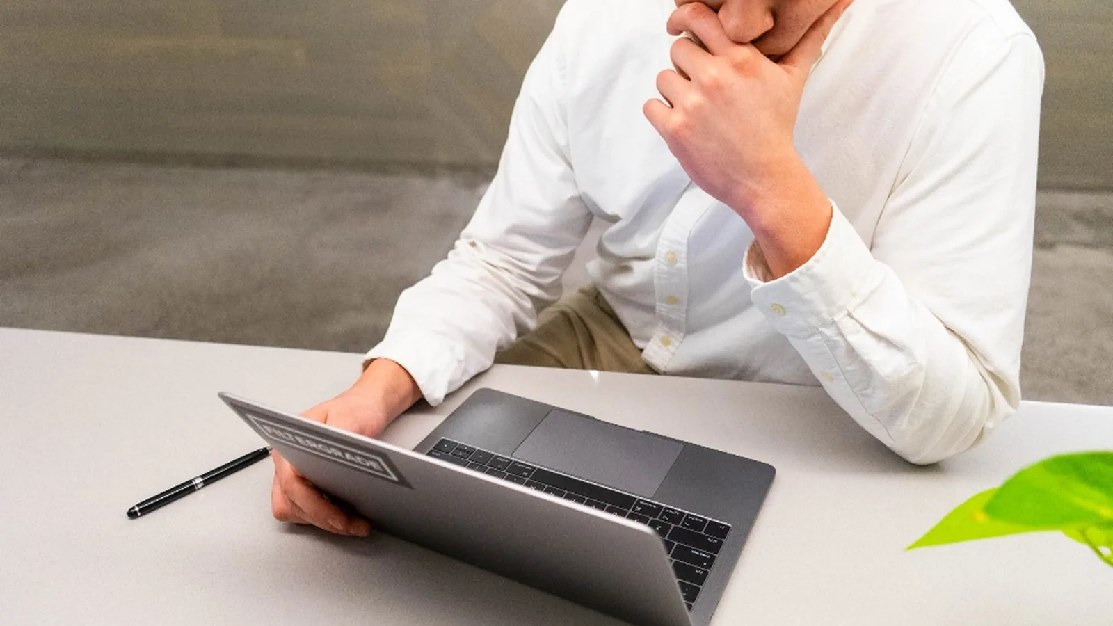 A man resting his hand against his jaw while working at a laptop