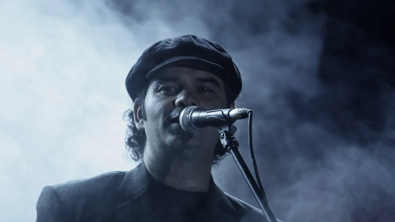 A singer at a microphone on a smoky stage, lit from behind