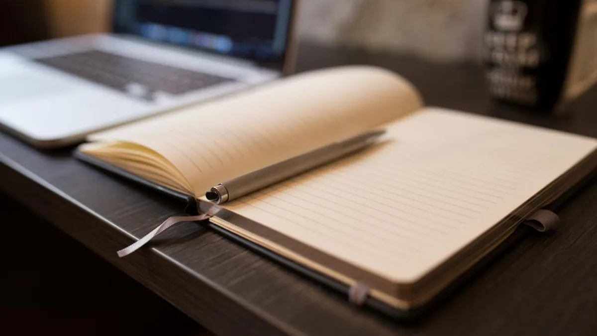 An open lined notebook with a pen lying across the page, on a desk