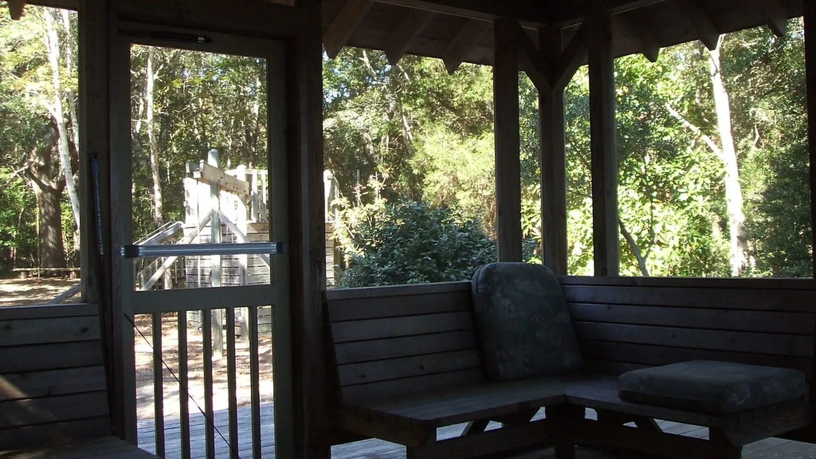 An empty covered porch with a chair, looking out onto trees in daylight