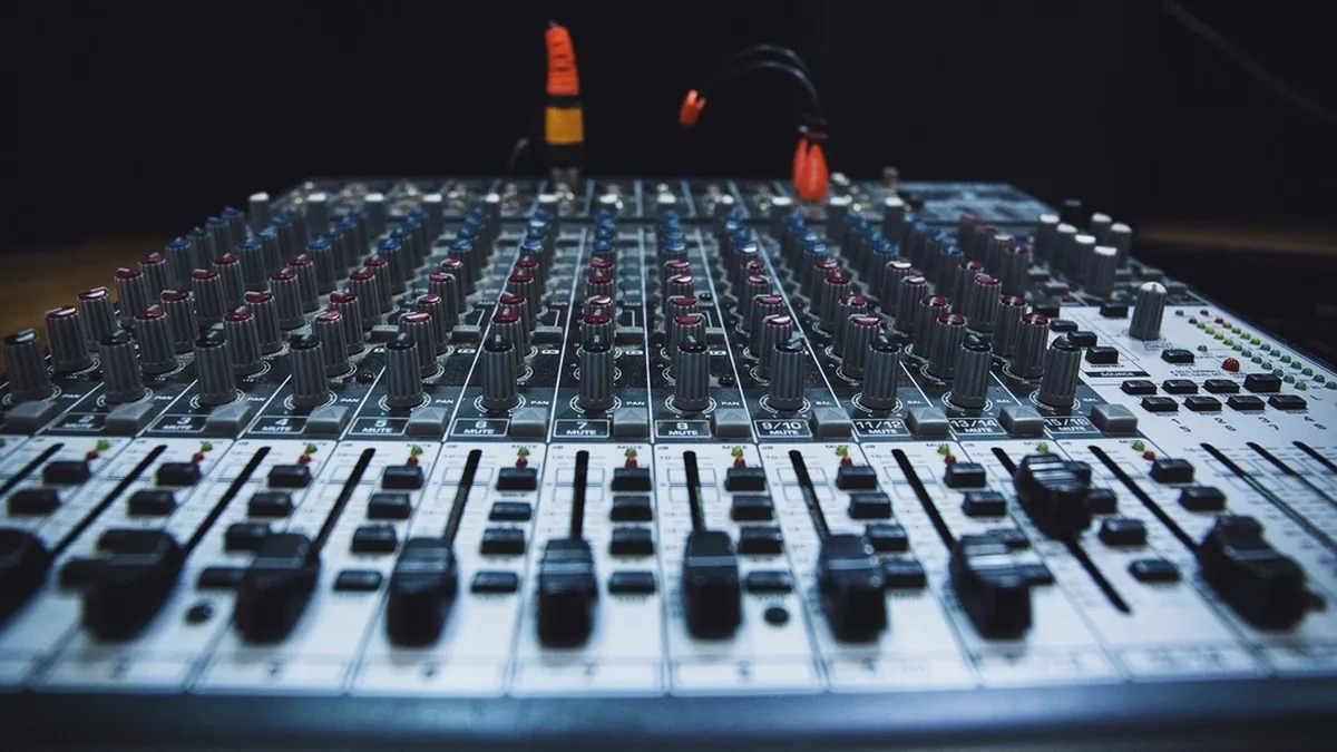 Close-up of a mixing console with rows of faders and knobs