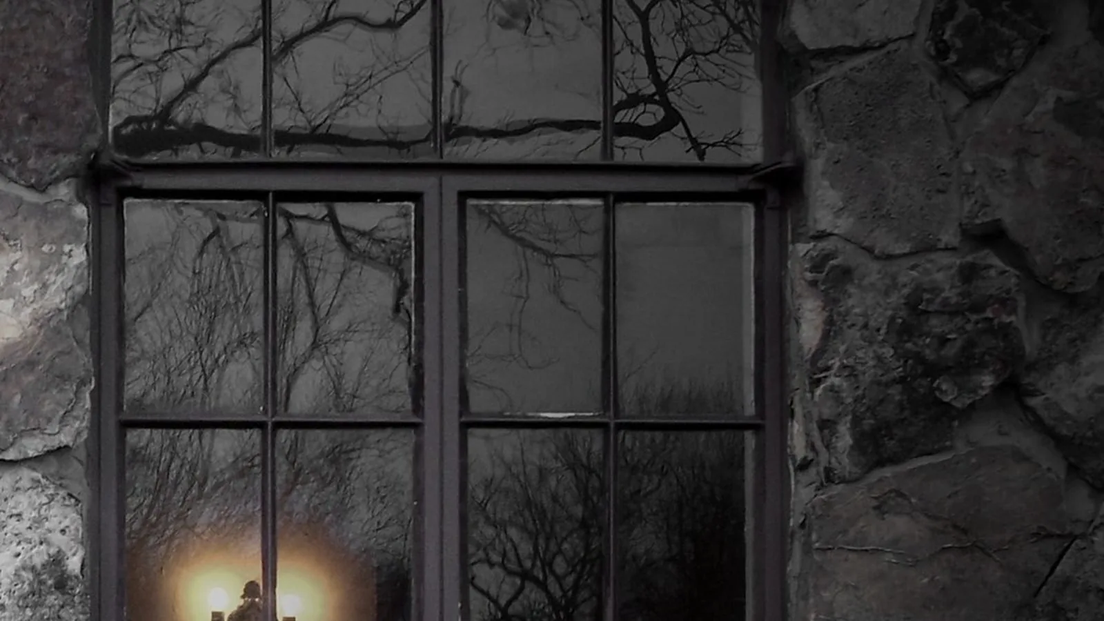 An old window at night seen from outside, with a single lamp lit inside