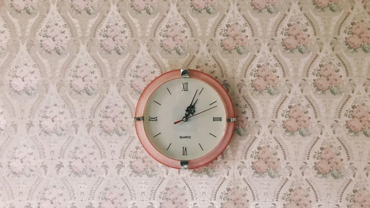 A round wall clock with a pink frame on floral wallpaper